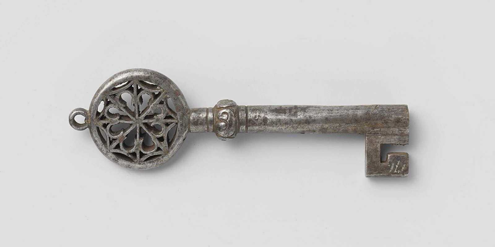 A single wrought-iron medieval key photographed flat on a pale grey ground, its bow pierced with tracery.