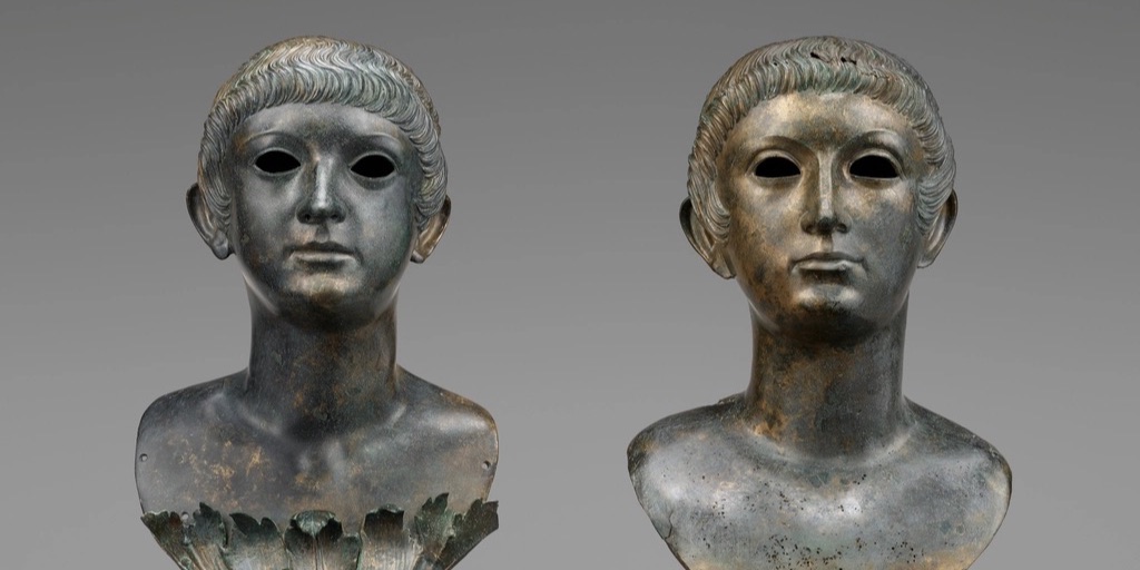 Two Roman bronze portrait busts of young men side by side, hollow-eyed, near-identical at a glance but clearly two different people.